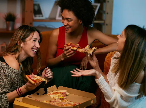 Trois femmes souriantes partageant une pizza dans un cadre convivial et chaleureux