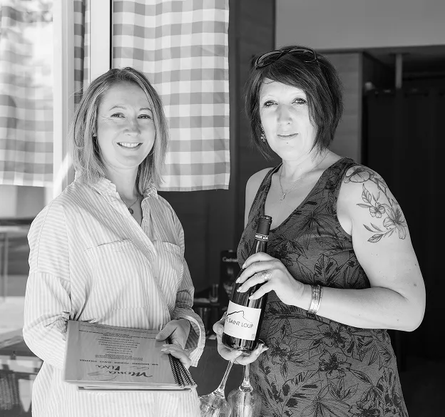 Deux femmes souriantes avec trophée et bouteille dans restaurant convivial